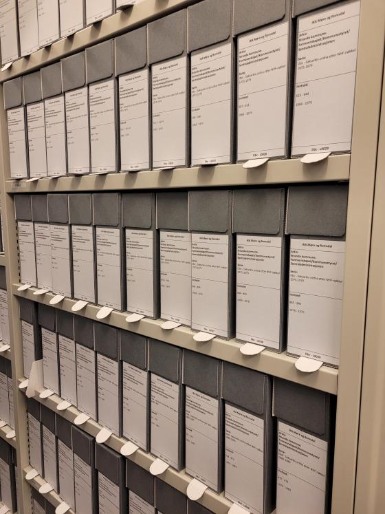 Ein ser inn i eit fag i ein arkivreol, der hylle på hylle er fylt med grå boksar med etikettar pålimt.