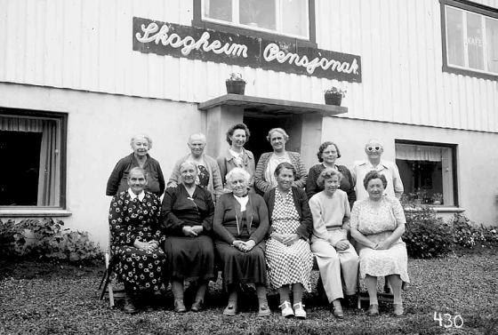 Ei lita gruppe kvinner oppstilt for fotografering framfor eit pensjonat.