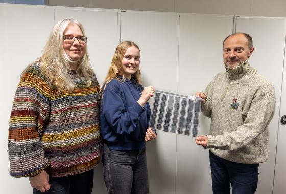 To kvinner og ein mann ser mot kamera, eine kvinna og mannen held negativar mellom seg