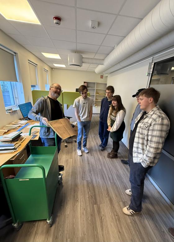 studentar står ved ein arbeidspult og får forklart ordning av privatarkiv