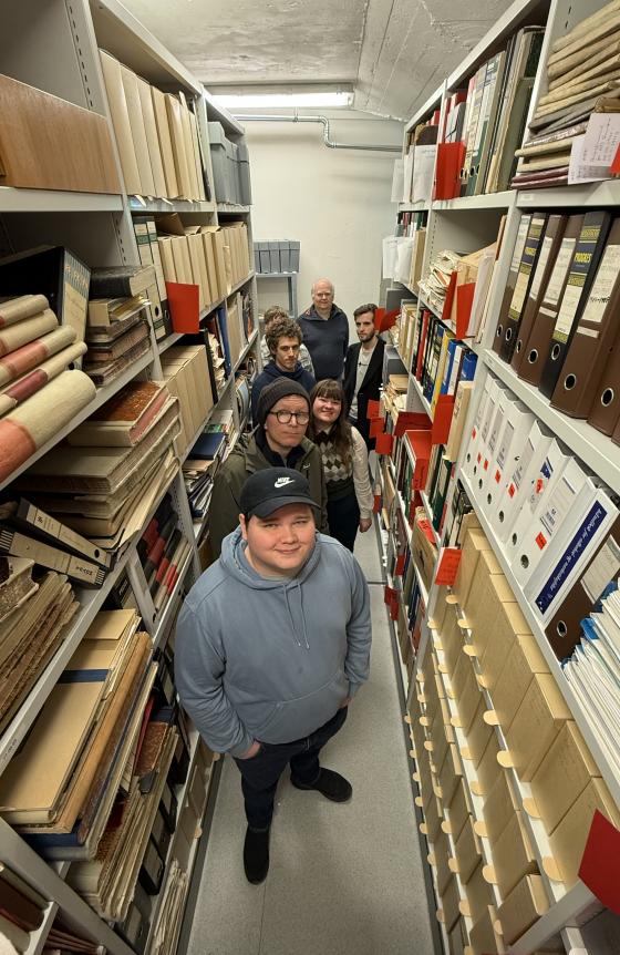 studentar står inne i ein arkivreol fylt med eldre arkiv