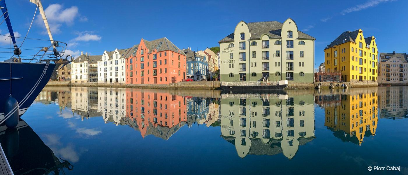 Bilde av fargerige hus i Brosundet, Ålesund, blå himmel og hus speglar seg i vatnet