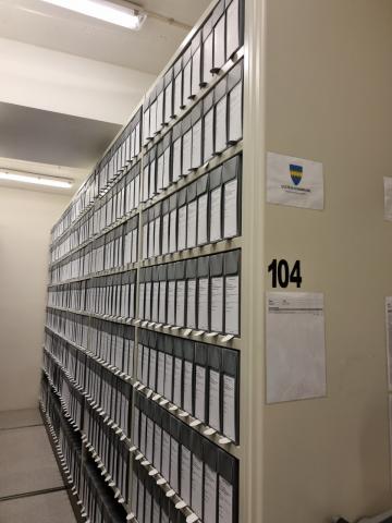 Ser inn i ein arkivreol fylt med grå arkivboksar med kvite etikettar