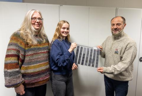 To kvinner og ein mann ser mot kamera, eine kvinna og mannen held negativar mellom seg