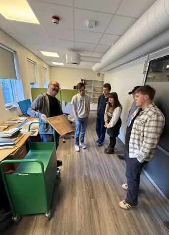 studentar står ved ein arbeidspult og får forklart ordning av privatarkiv