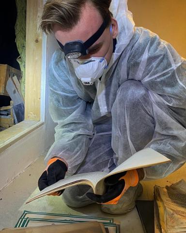 Ein mann med beskyttelsesutstyr som maske og dresss og hovudlykt ser på gamle dokument