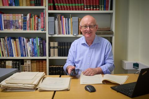 Ein eldre mann sit ved eit lesesalsbord og kikar gjennom gamle dokument